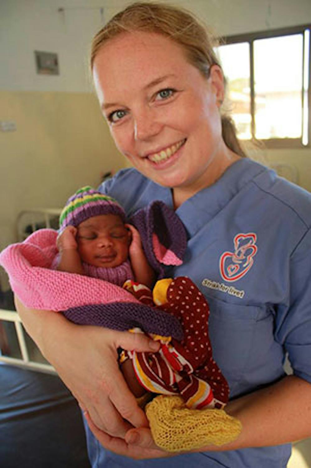Rebekka holder en nyfødt baby i strikket pledd