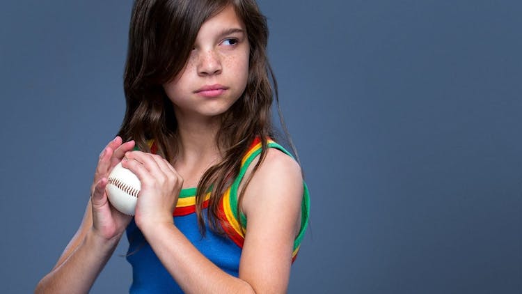 Ung jente i blå topp holder en baseball i begge hender