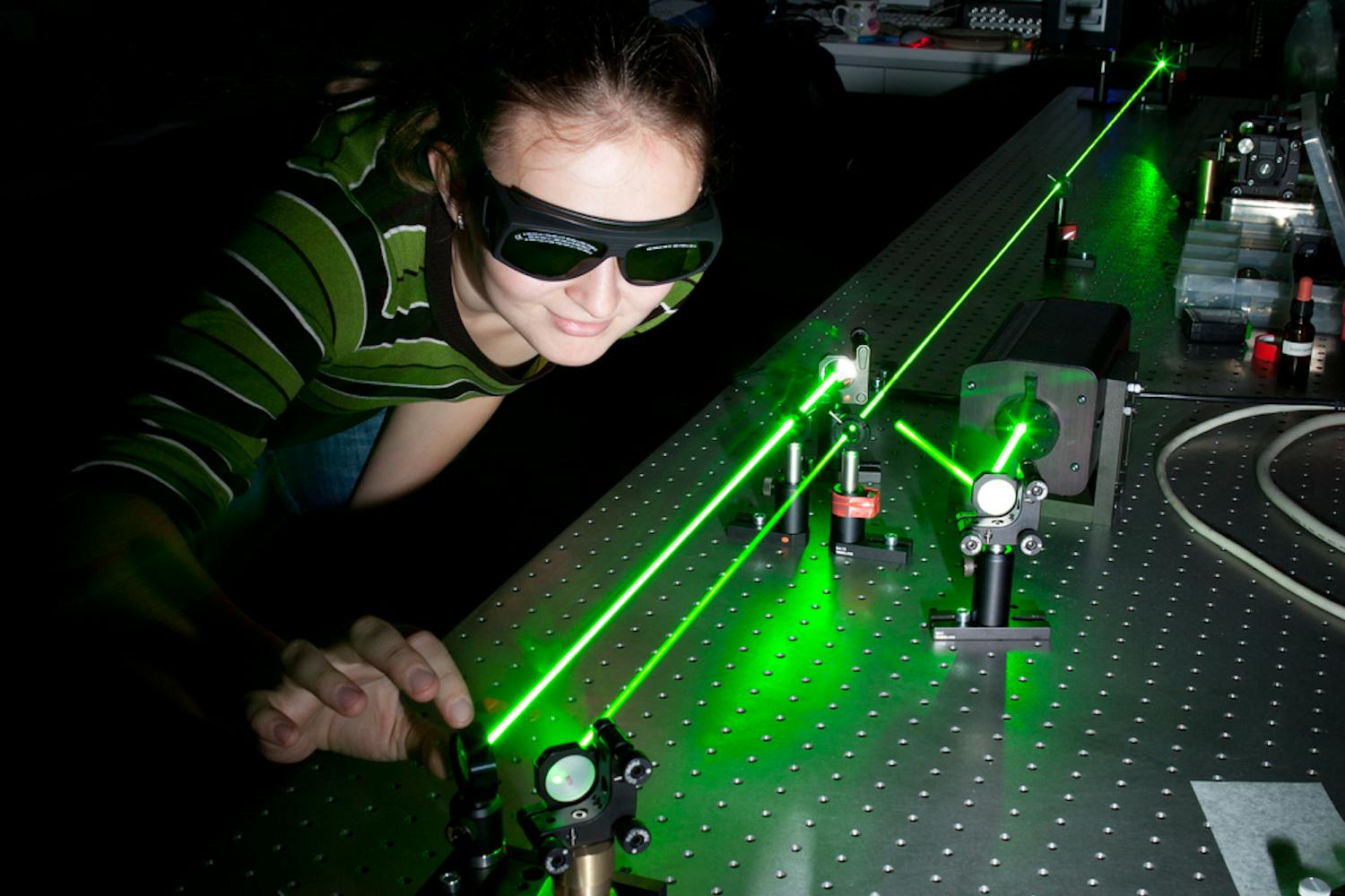 Jente med sikkerhetsbriller ser på grønn laserstråle og justerer refleksjonen til strålen