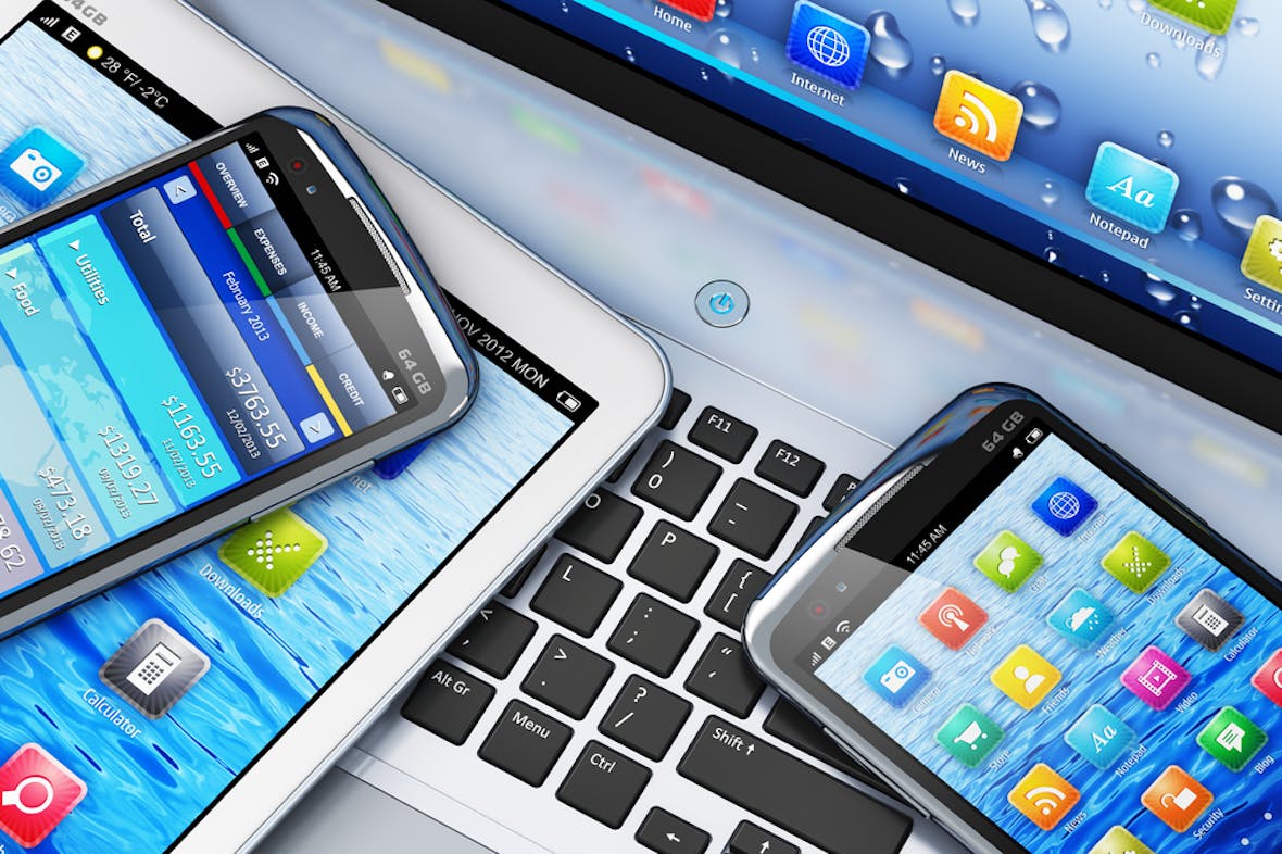 En tablet og to telefoner ligger på tastaturet til en laptop