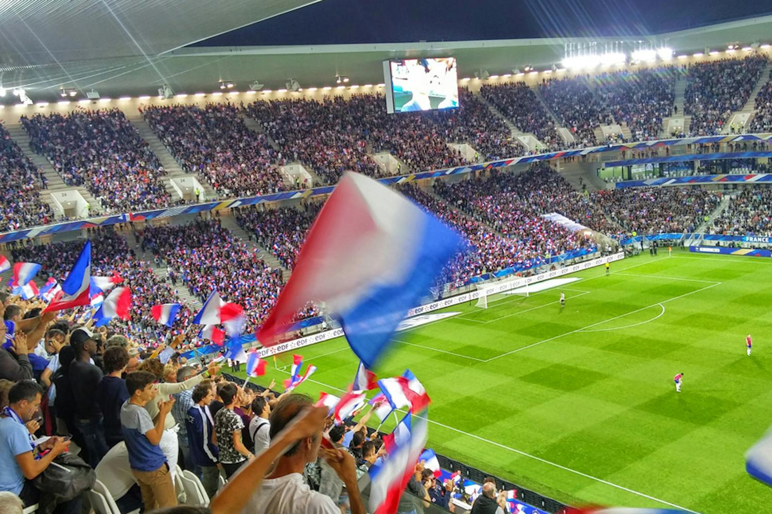 Full tribune av folk som vifter med franske flagg på fotballkamp