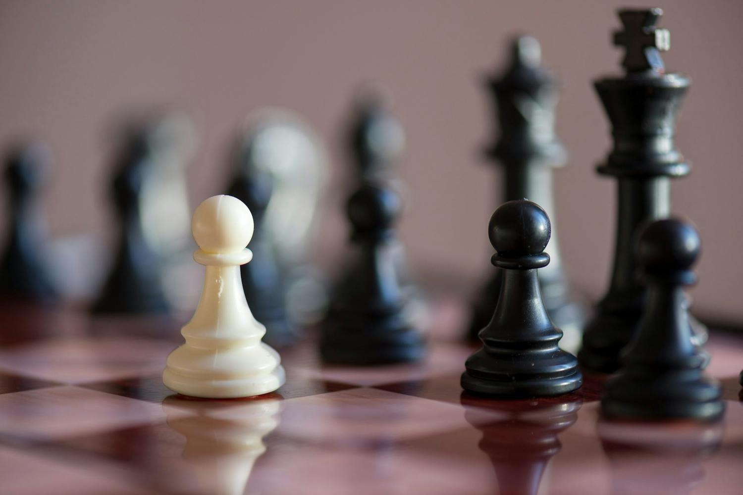 En hvit og en sort sjakkbonde på et sjakkbrett. I bakgrunnen er flere figurer