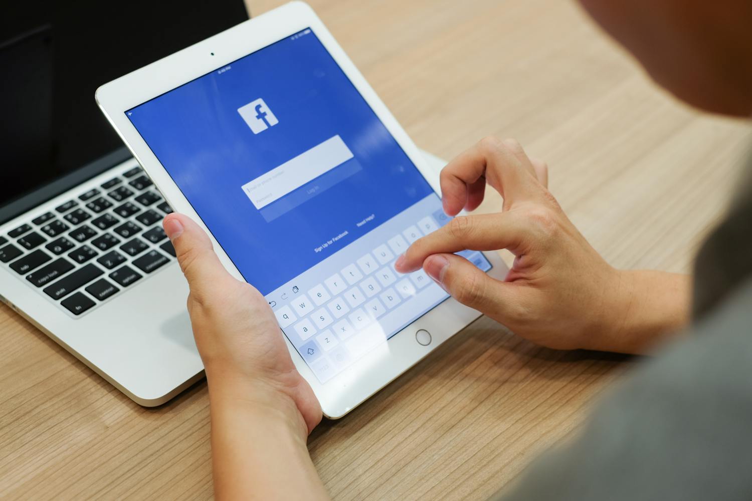 Person sitter foran laptop med ipad i hendene og logger inn på facebook