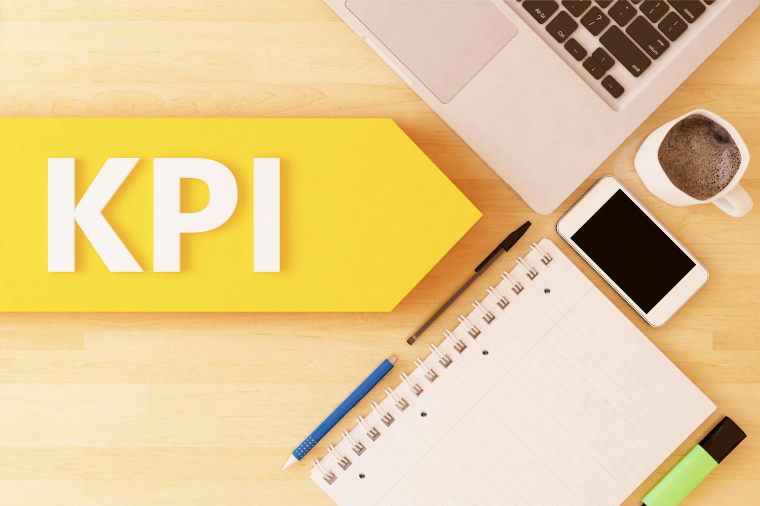 En gul pil med "KPI" i på et bord med notatblokk, penner, mobil, kaffe og laptop