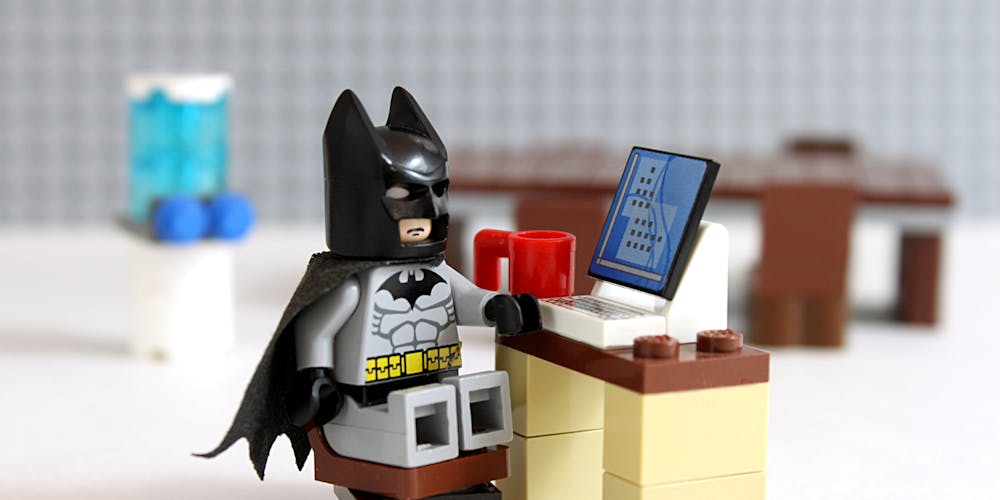 Lego Batman sitter på legostol foran legopult og data med kaffekopp