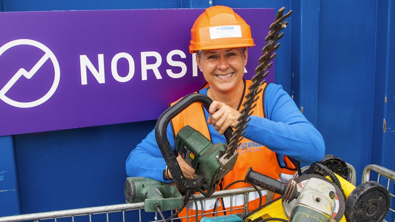 Guro Kjørsvik Husby, kommunikasjonsdirektør i Norsirk, har på oransje hjelm og holder oppe en elektrisk sag, mens hun smiler.