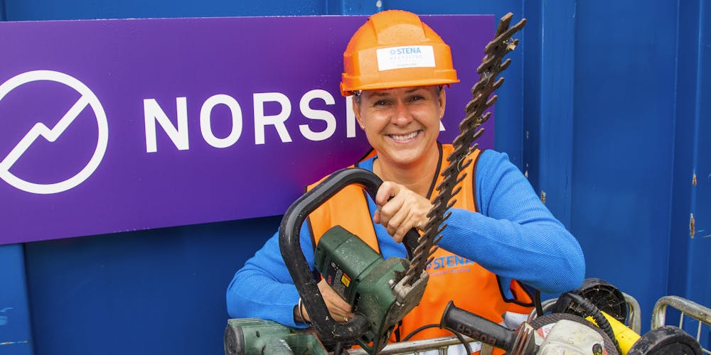 Guro Kjørsvik Husby, kommunikasjonsdirektør i Norsirk, har på oransje hjelm og holder oppe en elektrisk sag, mens hun smiler.