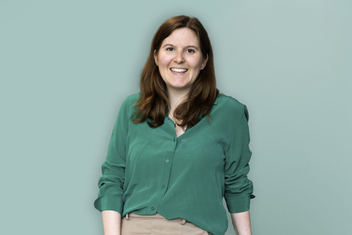 Martine Cecilie Vik står foran grønn bakgrunn og spør om vi skal bruke KI eller AI.